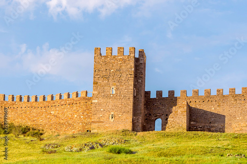 Ruins of the old tower Genoese fort fort a crenellated wall on top of a green hill An old stone building on a blue sky background. Crimea August 2017