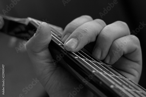 Male hand picks up a guitar chord. Guitar wrinkled male fingers pinch the strings on a black fingerboard. Black and white photo of playing the guitar.