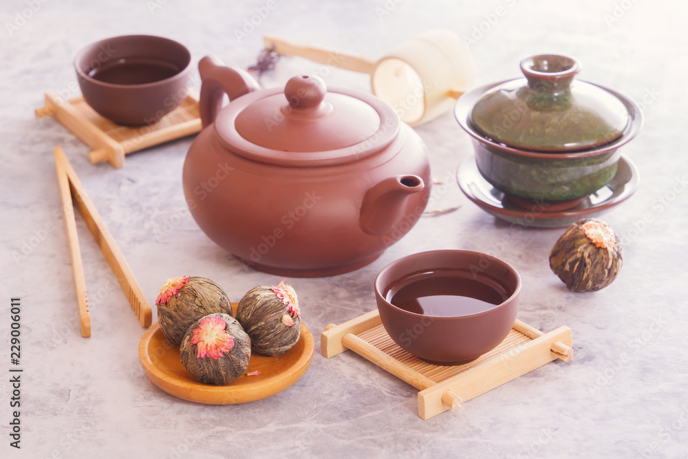 Green tea in buds, brown ceramic teapot with a cup prepared for a traditional Asian tea ceremony stand on a gray table Green tea in buds, brown ceramic teapot with a cup prepared for a traditional Asian tea ceremony stand on a gray table