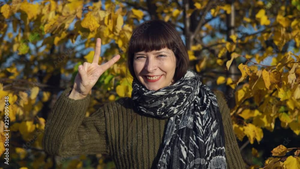 A young woman in a green knitted sweater shows a victoria sign against the background of yellow foliage in a city park in Indian summer. A young woman in a green knitted sweater shows a victoria sign against the background of yellow foliage in a city park in Indian summer.