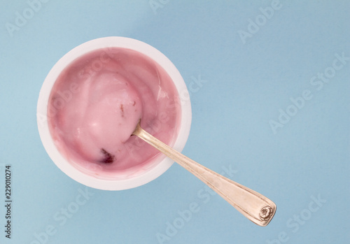 Yogurt in plastic cup close up with small silver spoon, top view photo of strawberry yoghurt on pale blue background