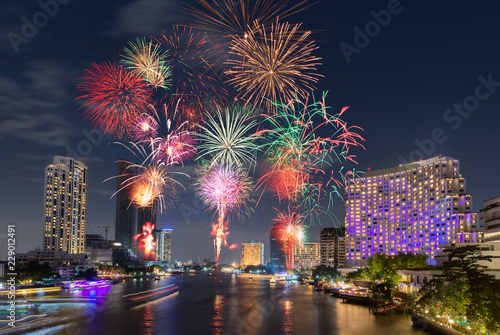 New Year Fireworks at midnight over clear sky above river city surrounding with luxury hotels, restaurants, condominiums, shopping mall in main city for special happy holiday celebration event