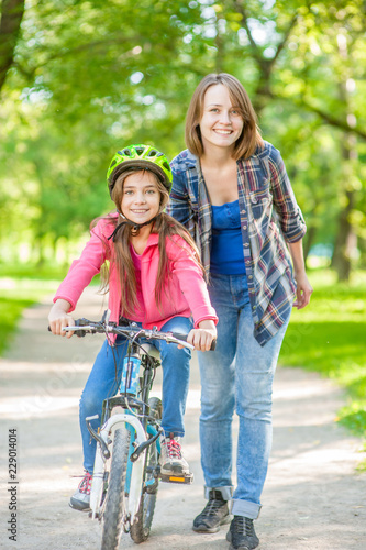 Smiling mom teaches her daughter to ride a bicycle in the park