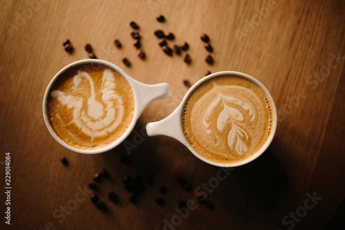 Two latte coffee cups with a drawing on a wooden table 