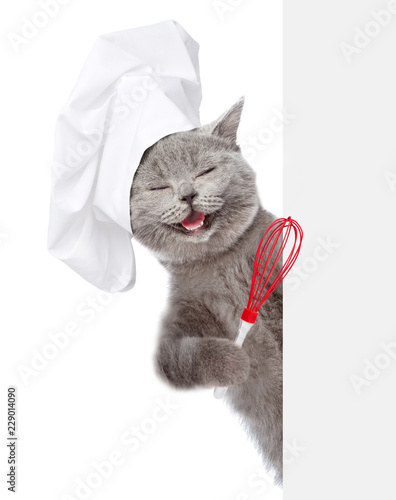 Szczęśliwy kot w kapeluszu szefa kuchni trzymając drucianą trzepaczką nad białym sztandarem. na białym tle