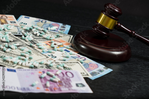 Wood judge's gavel and scattered colorful drugs on the dollar and euro cash background