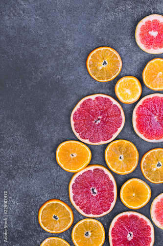 Fresh oranges, grapefruits and madarine slices on dark stone background. © oxxyzay