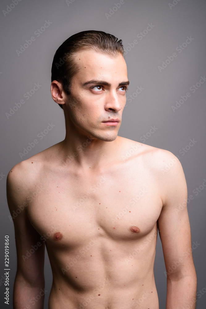 Fototapeta premium Young handsome man shirtless thinking and looking up against gray background