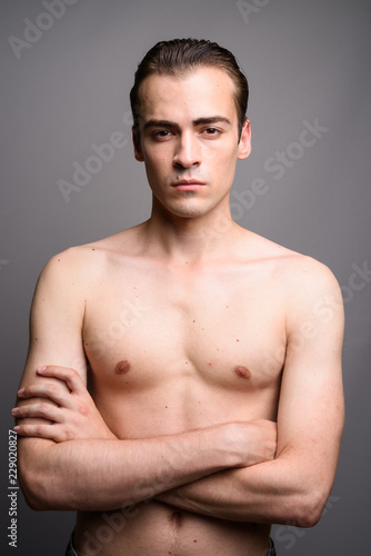 Young handsome man shirtless with arms crossed against gray background