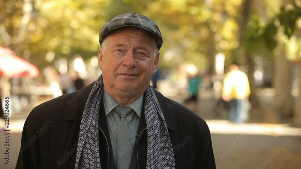 Bokeh portrait of a stylish old man in a plaid flat cap, business suit, necktie and long jacket smiling in a golden park in autumn Bokeh portrait of a stylish old man in a plaid flat cap, business suit, necktie and long jacket smiling in a golden park in autumn