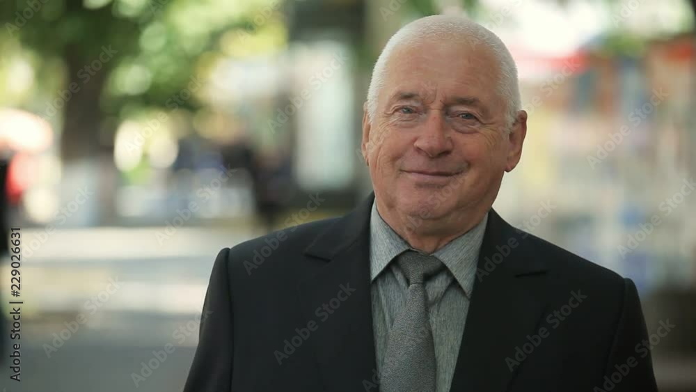 Emotional bokeh portrait of a wise old man in a tidy black business suit standing and smiling happily in a green park in autumn Emotional bokeh portrait of a wise old man in a tidy black business suit standing and smiling happily in a green park in autumn