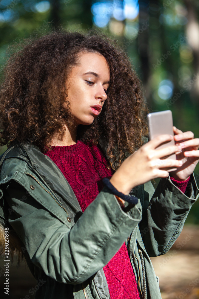 Φωτογραφία Cute curly hair teen girl with smartphone in autumn forest