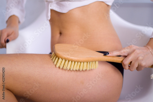 Cosmetology, grooming, Spa cosmetic products, beauty and bikini concept. closeup Woman in black panties makes massage legs with wooden soft massage brush for body and legs