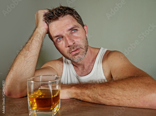 young wasted and depressed alcohol addict man in dirty singlet drinking glass of whiskey feeling desperate suffering alcoholism problem and booze addiction in alcoholic concept