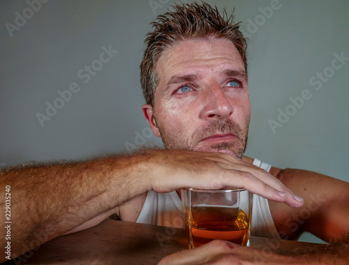 young wasted and depressed alcohol addict man in dirty singlet drinking glass of whiskey feeling desperate suffering alcoholism problem and booze addiction in alcoholic concept