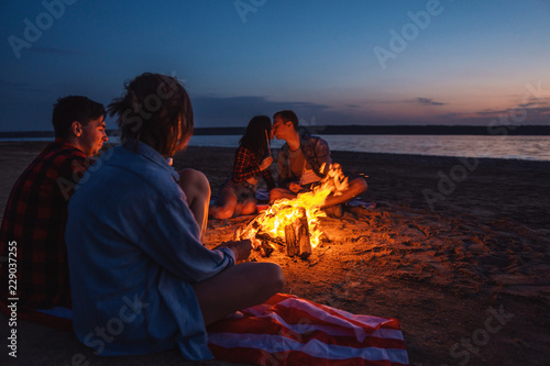 Camp on the beach. Group of young friends having picnic with bonfire. One couple is kissing