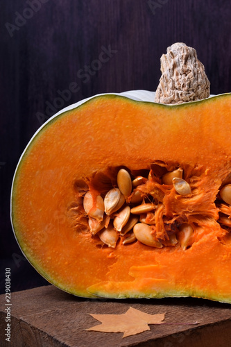 Fotografie Half of a pumpkin with orange flesh on a wooden board surrounded by dry maple le