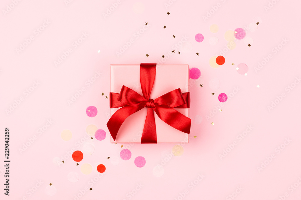 Pink gift box with red bow on pink background with sparkles. Holiday concept.
