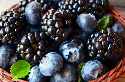 Fresh ripe organic blueberries and blackberries in a basket on old wooden table close up.Healthy eating,vegan food or diet concept.Selective focus.