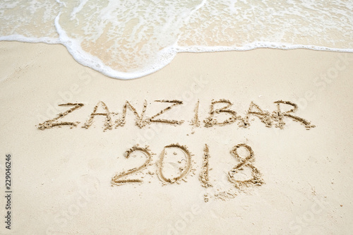 zanzibar script on light sand and ocean wave