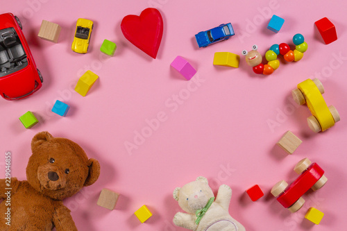 Baby kids toys frame with teddy bear, wooden toy car, colorful bricks on pink background. Top view