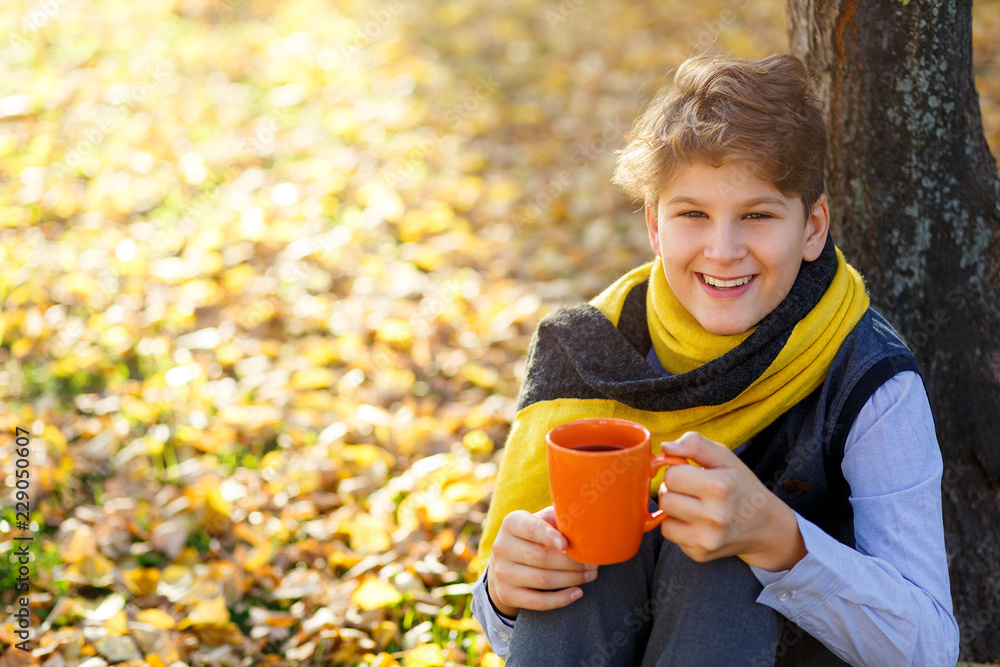 boy with yellow scarf holds orange cup in hands on fallen leaves background. autumn mood beautiful day. Golden fall in still life. Bright Fall image. boy with yellow scarf holds orange cup in hands on fallen leaves background. autumn mood beautiful day. Golden fall in still life. Bright Fall image.