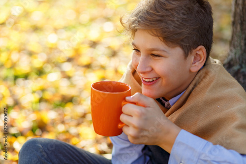 boy with yellow scarf holds orange cup in hands on fallen leaves background. autumn mood beautiful day. Golden fall in still life. Bright Fall image.  