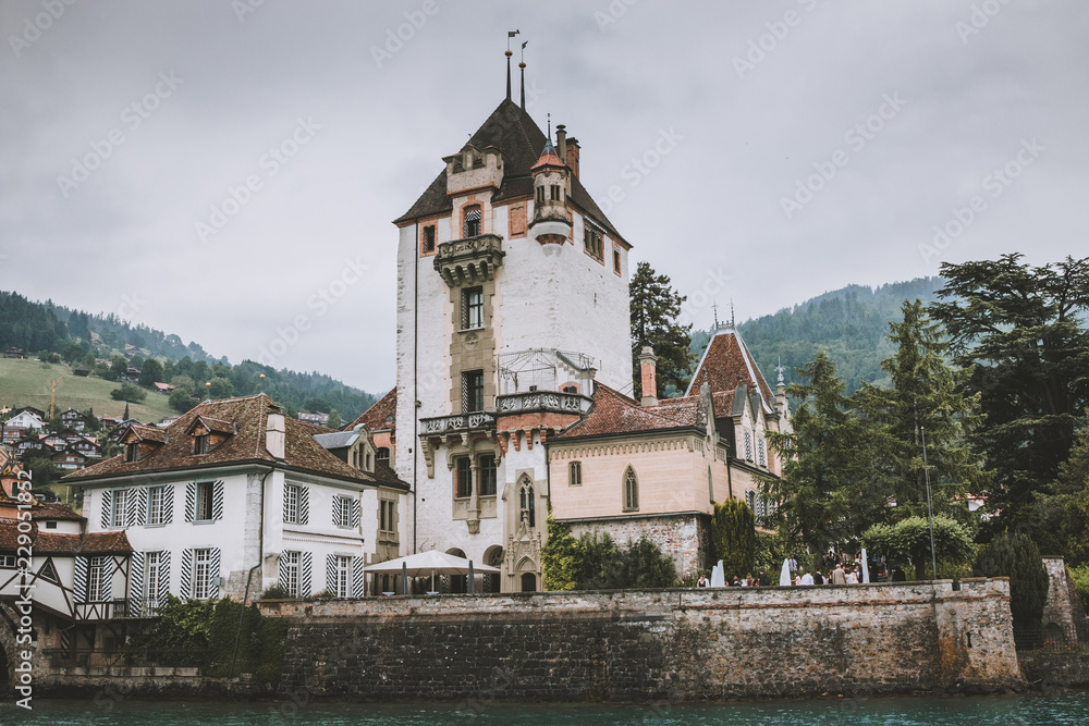 Oberhofen, Switzerland - June 22, 2017: View on Oberhofen Castle - living museum and park from ship, Switzerland, Europe. Summer landscape, cloudy weather, dramatic sky and sunny day. Print photo