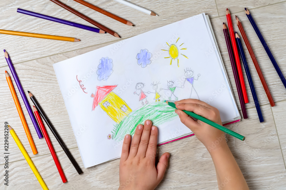 Naklejka premium The child draws his family on a piece of paper with colored pencils. What can a children's picture tell. The concept of child psychology.