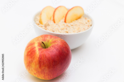 Oatmeal in white bowl and red apple on white background. Isolated on white. Healthy food