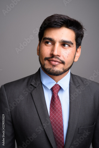Young handsome bearded Persian businessman against gray backgrou