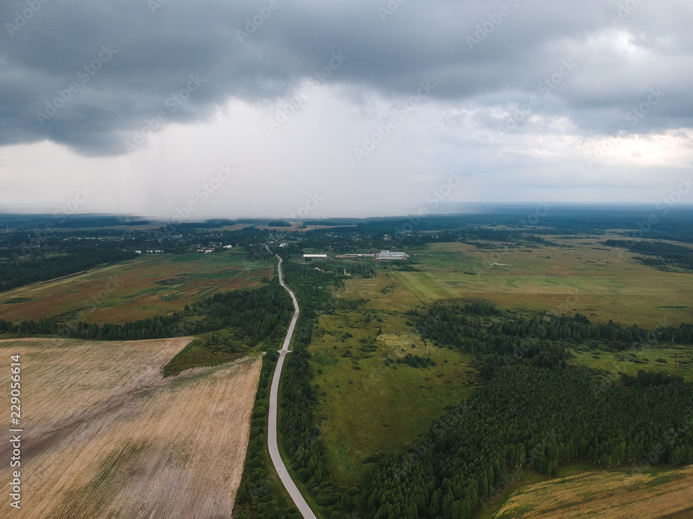 view of the road to a huge cloud with rain from the height of the quadrocopter, around the road forests and fields