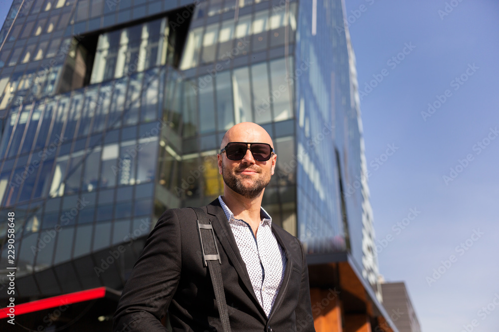 Fototapeta premium Handsome elegant businessman with sunglasses in front of office building