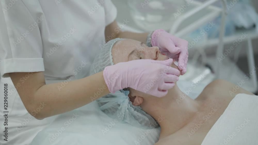 The hands of the cosmetologist make a scrub the face of the patient The hands of the cosmetologist make a scrub the face of the patient
