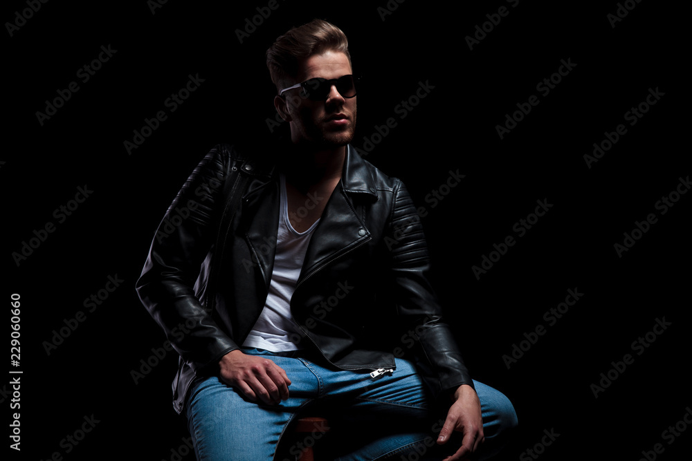 man in leather jacket sits and looks up to side