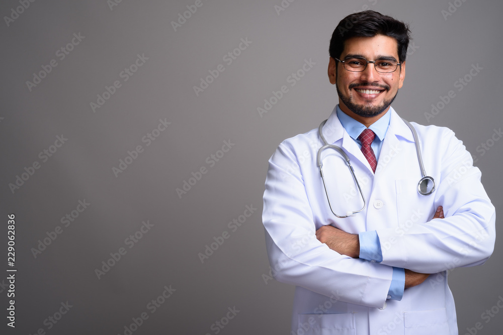 Young handsome bearded Persian man doctor against gray backgroun Young handsome bearded Persian man doctor against gray backgroun