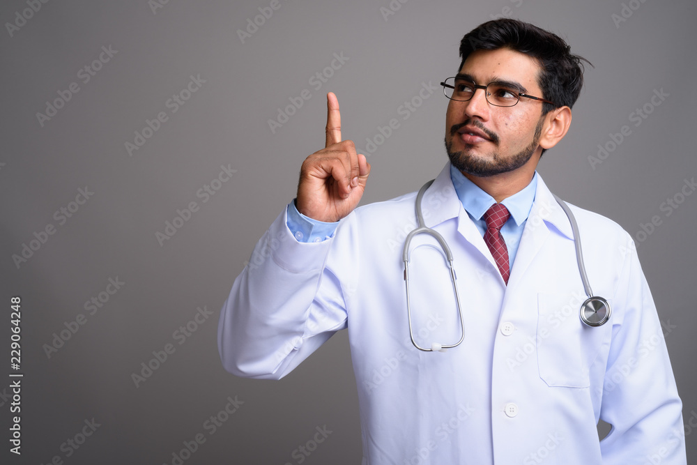 Young handsome bearded Persian man doctor against gray backgroun Young handsome bearded Persian man doctor against gray backgroun