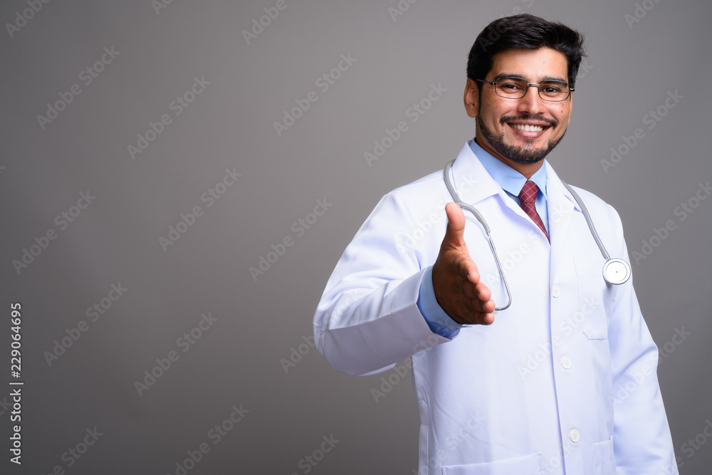 Young handsome bearded Persian man doctor against gray backgroun Young handsome bearded Persian man doctor against gray backgroun