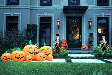 The house is decorated for Halloween:Many different pumpkins with faces and two dead man butlers with signs in their hands. Night, Houston, Texas, United States