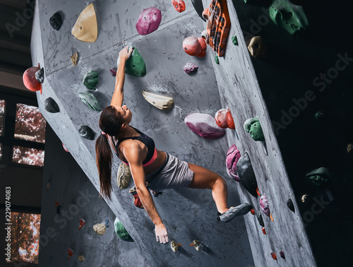 Professional female climber hanging on the bouldering wall, practice climbing indoors.