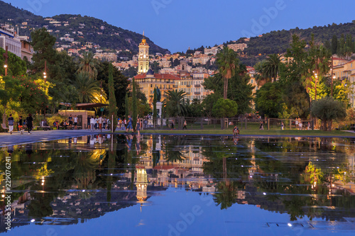 Nice, Cote d'Azur. Fountains on Massena place. View to the old city and mountains from Massena place with working fountains in summer. Reflection in water. Travel France.