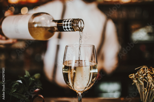 Close up shot of a bartender pouring white wine into a glass. Hospitality, beverage and wine concept.
