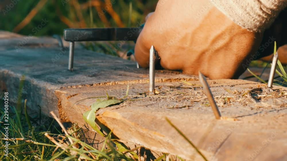 Man bends iron nails with pliers on an old board Man bends iron nails with pliers on an old board