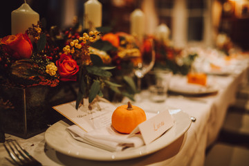 Thanksgiving table setting with automnal decorations, pumpkins, glasses and plates. Holidays, catering and hospitality concept.