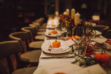 Thanksgiving table setting with automnal decorations, pumpkins, glasses and plates. Holidays, catering and hospitality concept.