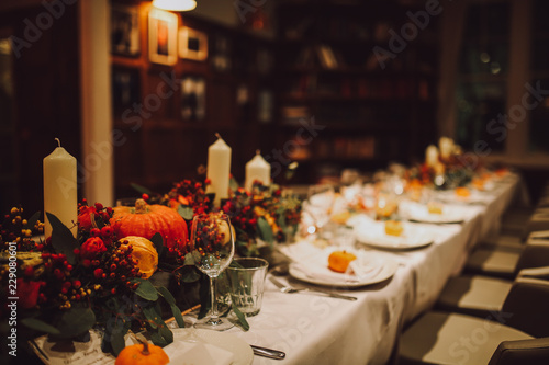 Thanksgiving table setting with automnal decorations, pumpkins, glasses and plates. Holidays, catering and hospitality concept.