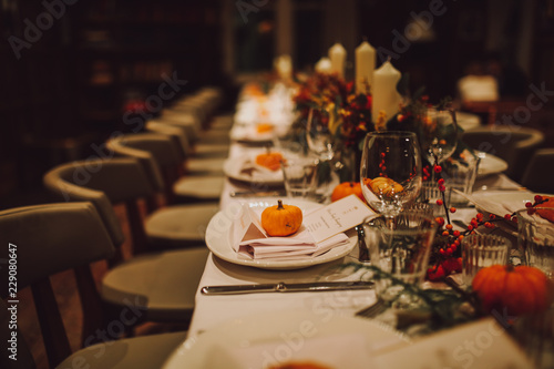 Thanksgiving table setting with automnal decorations, pumpkins, glasses and plates. Holidays, catering and hospitality concept.