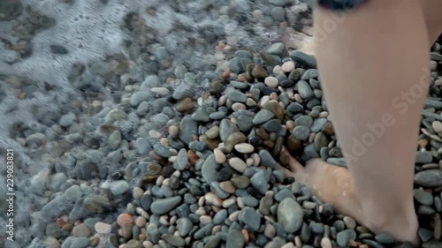 Girl walking on the beach with small colored stones of her legs in the sea