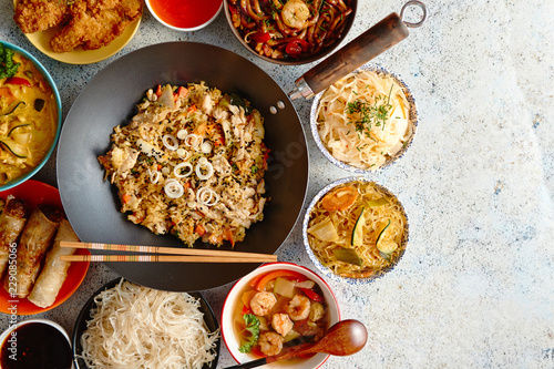 Traditional Chinese or Thai food set. Chinese noodles, fried rice with chicken, tom yum soup, spring rolls, deep fried fish and udon with shrimps. Top view. Asian style food concept.