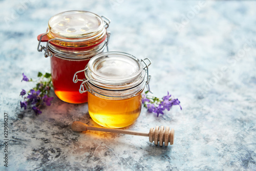 Jars with different kinds of fresh organic honey placed in a row on a blue stone background